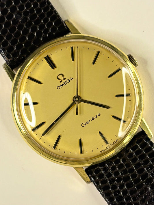 Omega Geneva analog watch with a gold-toned dial, gold case, and a textured black leather strap, shown on a plain light background.