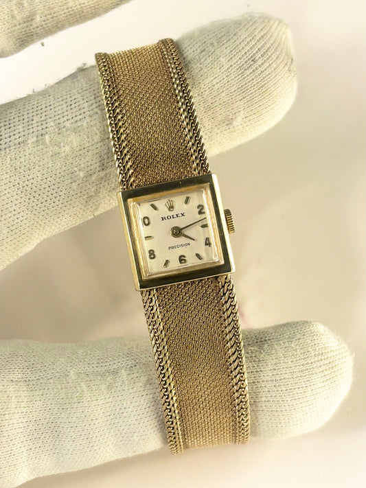 A vintage Rolex Precision watch with a gold-tone mesh bracelet and square dial, displayed on a white textured fabric surface.
