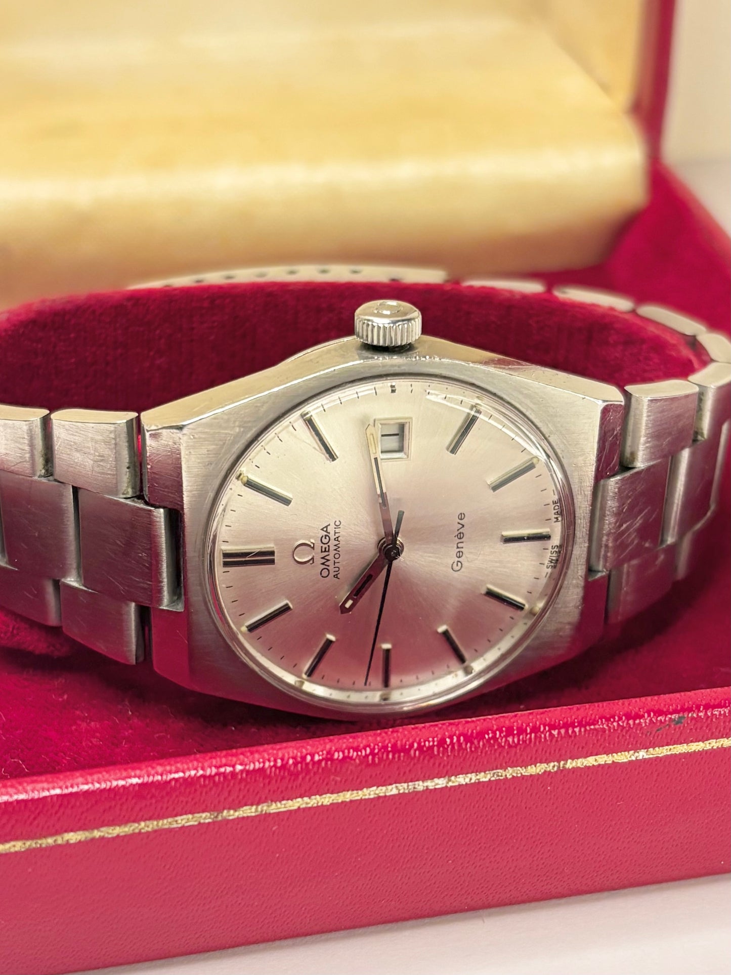 A vintage Omega Automatic wristwatch with a silver-toned metal bracelet and dial, resting inside a red velvet-lined watch box.