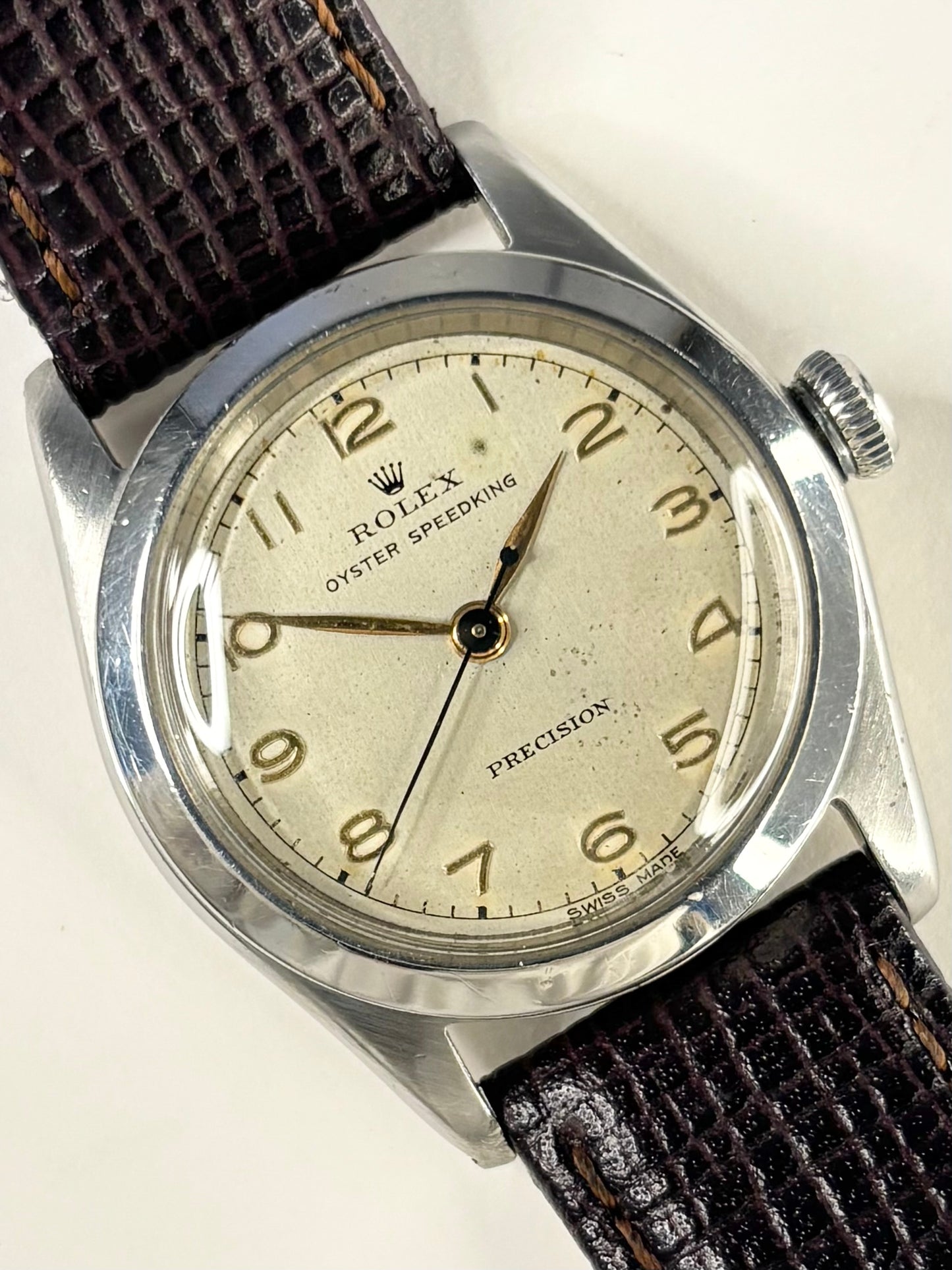 A vintage Rolex Oyster Speeding Precision watch with a silver-toned metal case, a cream-colored dial with gold-tone Arabic numerals, and a dark brown textured leather strap.