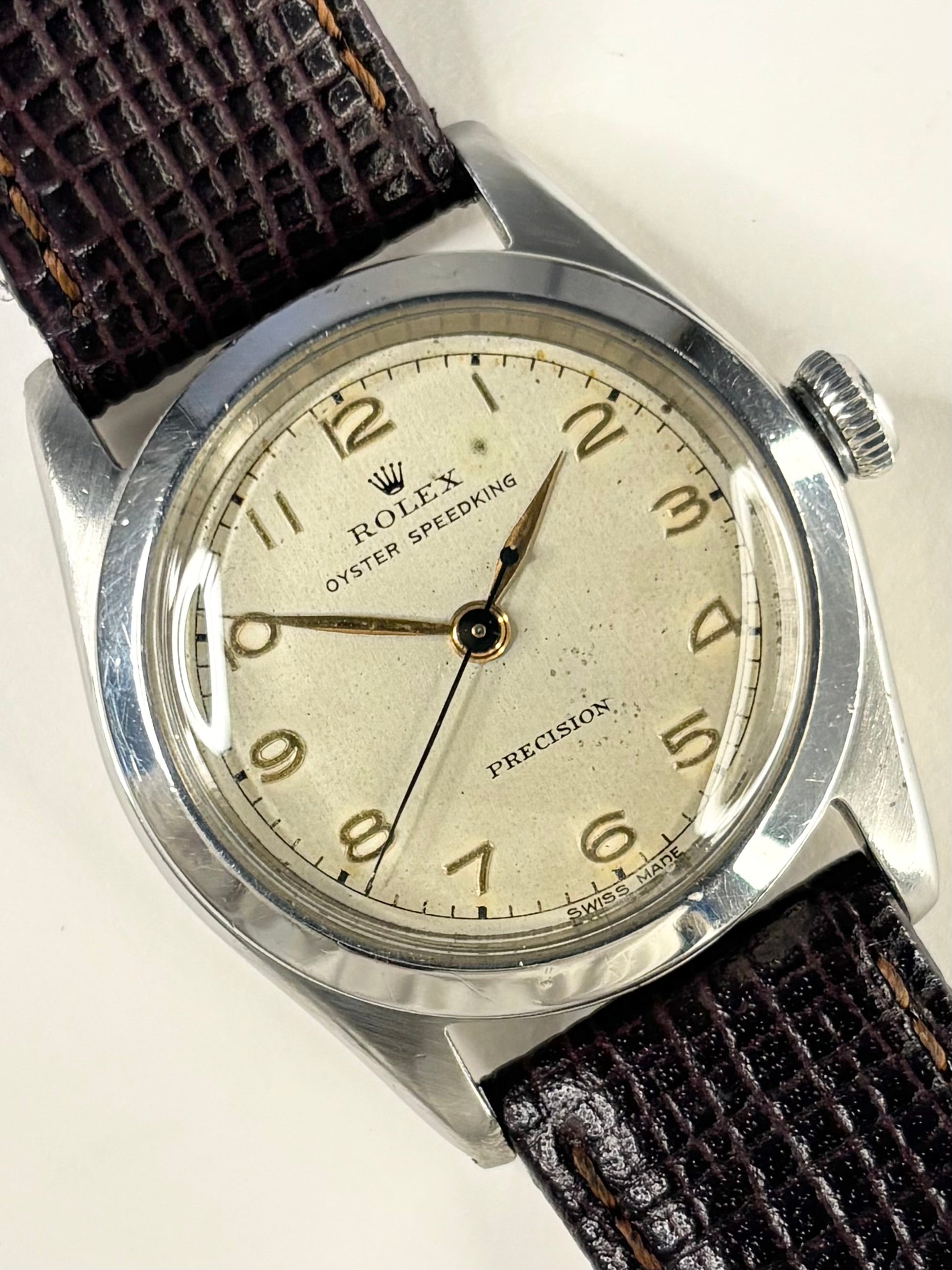 A vintage Rolex Oyster Speeding Precision watch with a silver-toned metal case, a cream-colored dial with gold-tone Arabic numerals, and a dark brown textured leather strap.