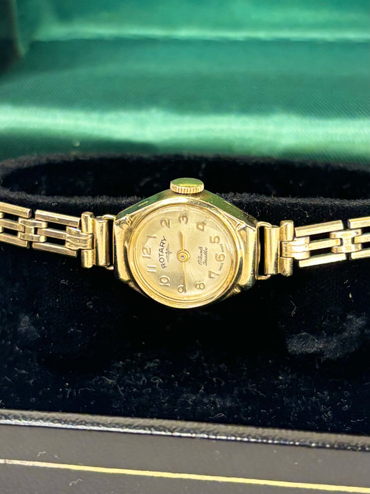 A vintage gold-tone wristwatch with a matching metal link bracelet, resting on a black velvet surface inside a green satin-lined box.