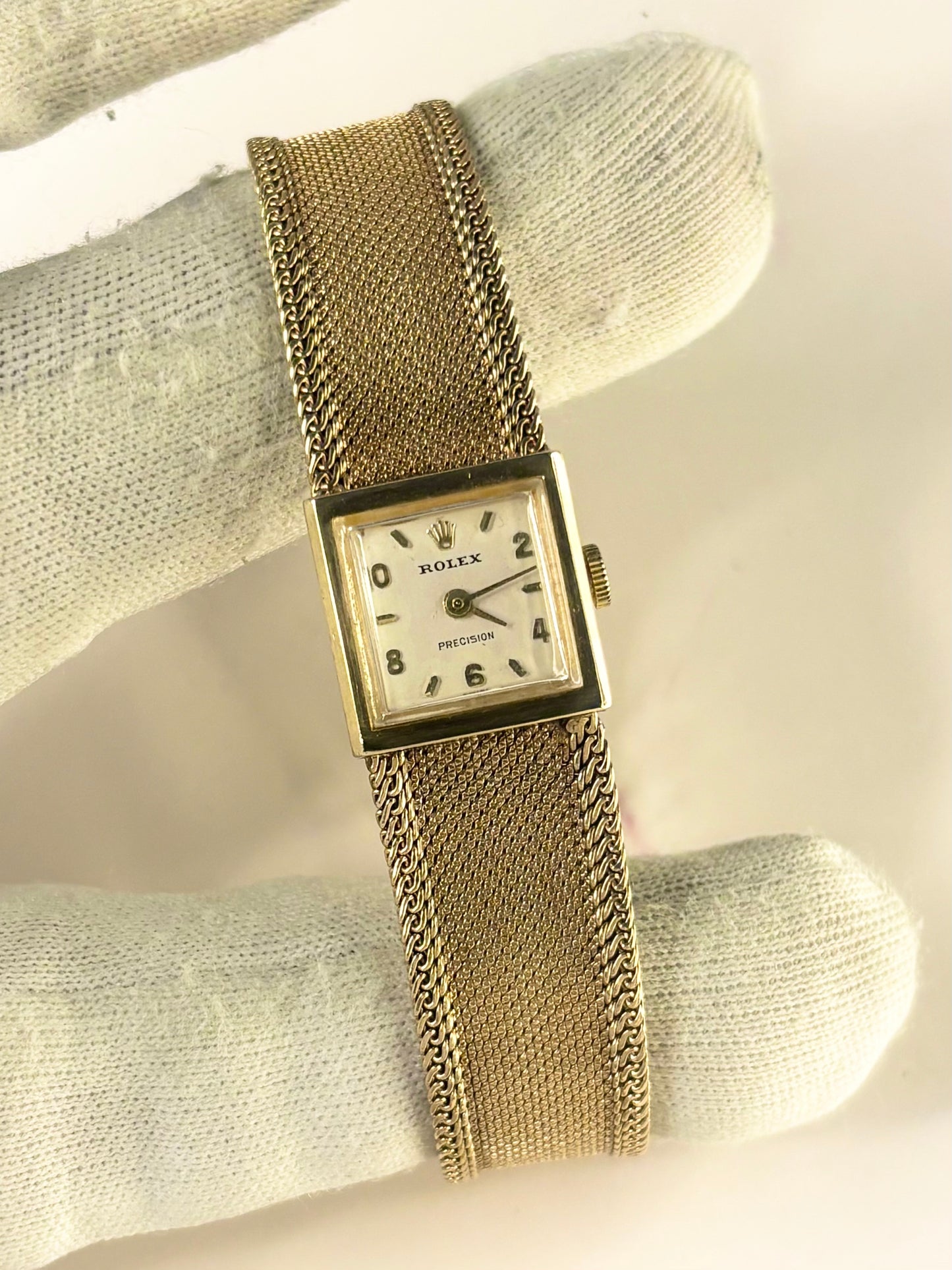 A vintage Rolex Precision watch with a gold-tone mesh bracelet and square dial, displayed on a white textured fabric surface.