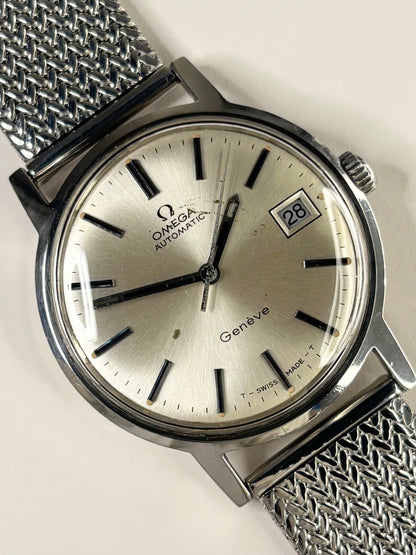 Omega Automatic Geneve wristwatch with a silver dial, black stick indices, and a silver mesh strap on a light background.