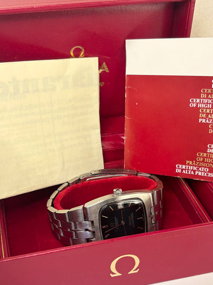 An Omega wristwatch with a stainless steel link bracelet and a black dial, displayed inside its red presentation box with certificates and papers.