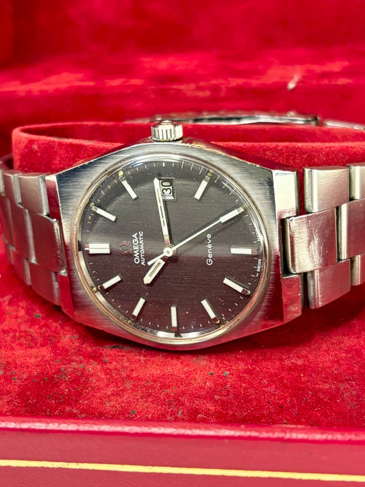 A vintage Omega x Swatch Genedive wristwatch with a brushed silver-tone metal bracelet and a dark dial, displayed inside a red velvet-lined box.