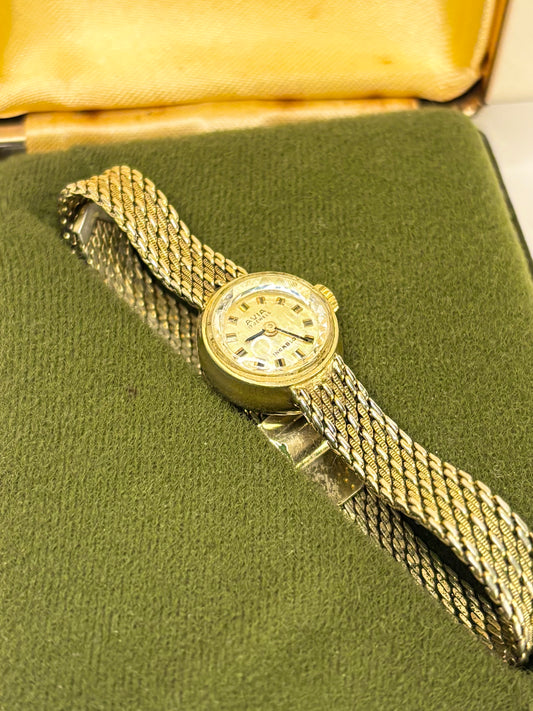 A vintage gold-tone avia women's watch with a mesh bracelet, resting on a green velvet watch box with a yellow satin interior.